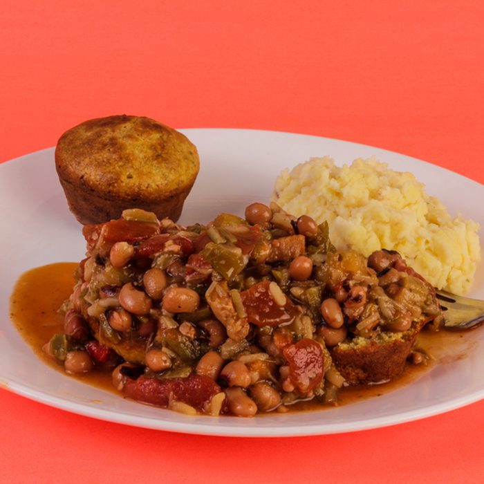 Creole Chicken Gumbo on white plate with mashed potatoes and cornbread against red background.