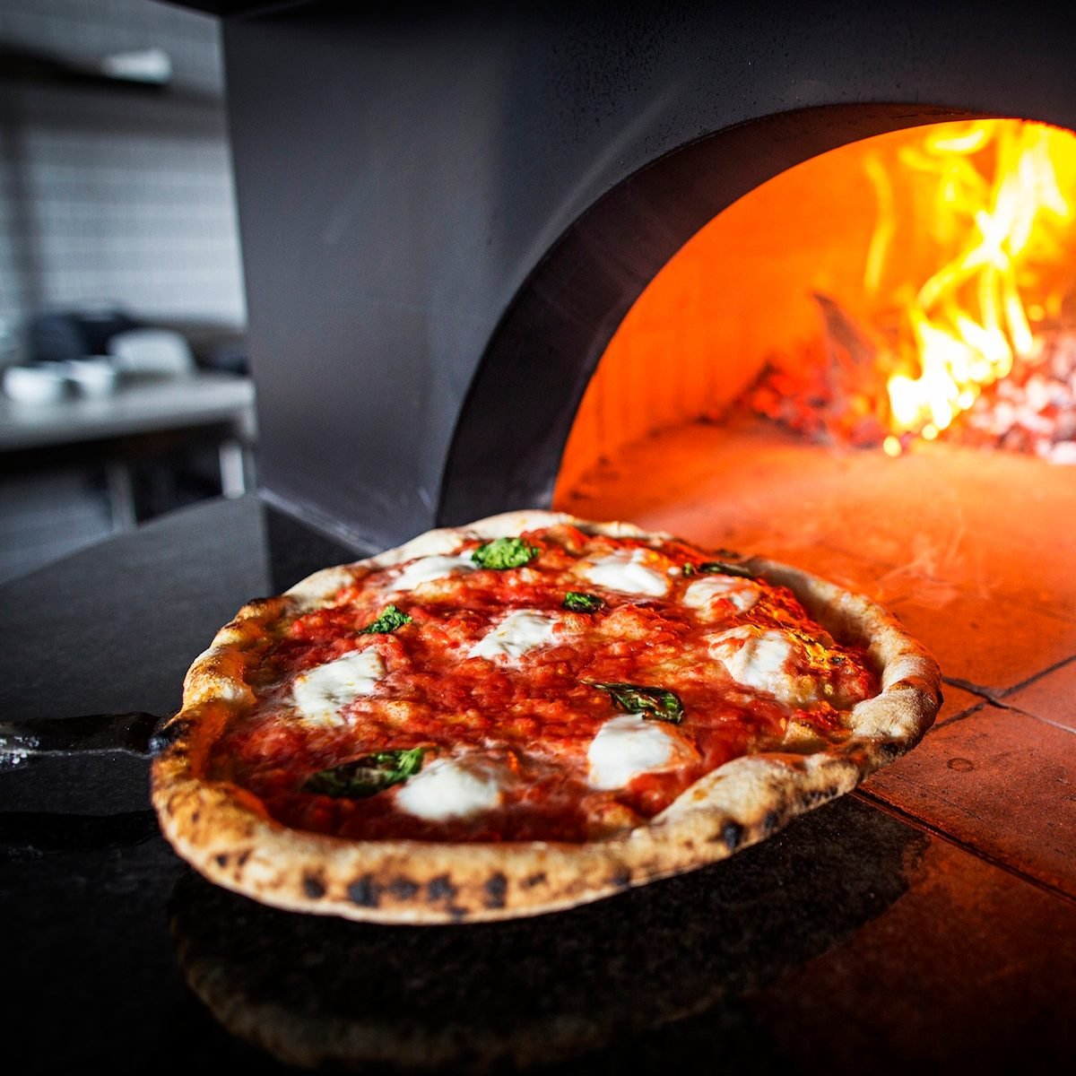 putting a pizza in a wood burning stove at Inferno Pizza