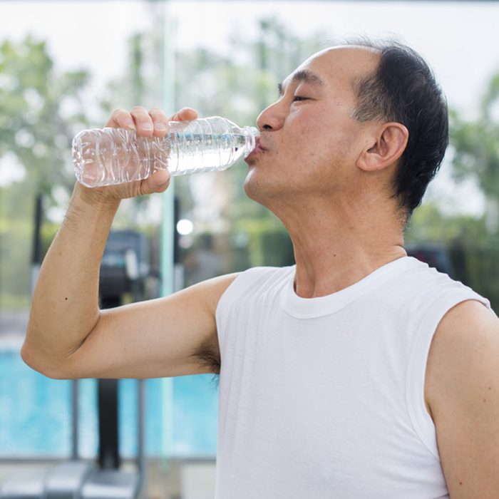 Senior asian man drinking water from a plastic bottle and background blur diverse equipment and machines at the gym room.