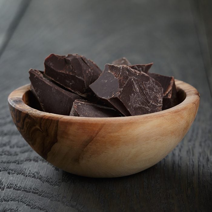 dark chocolate chunks in wooden bowl, on oak table;
