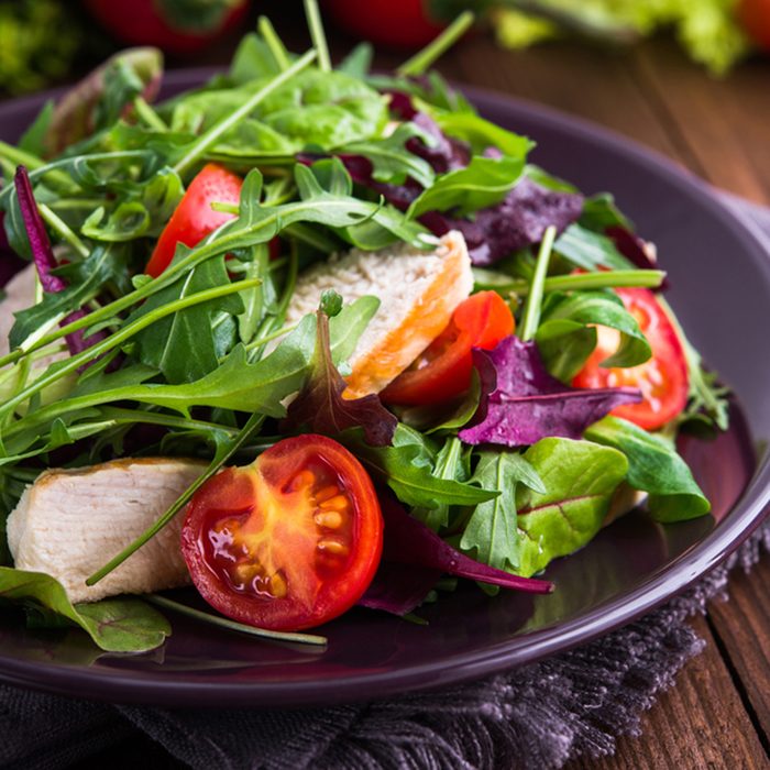 Fresh salad with chicken, tomatoes and mixed greens (arugula, mesclun, mache) on wooden background close up.