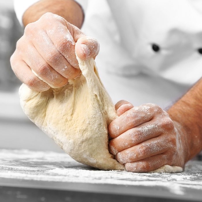 Male hands preparing dough for pizza on table closeup