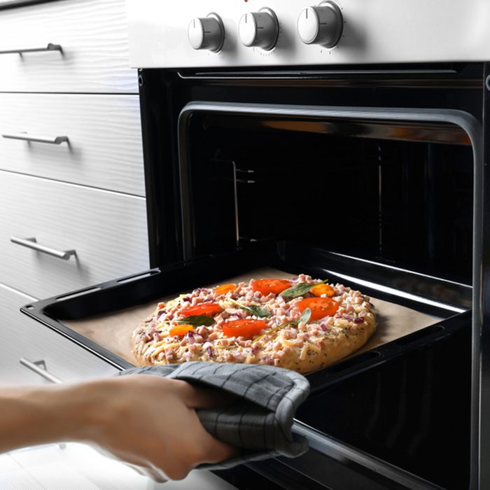 Woman putting baking sheet with pizza in oven