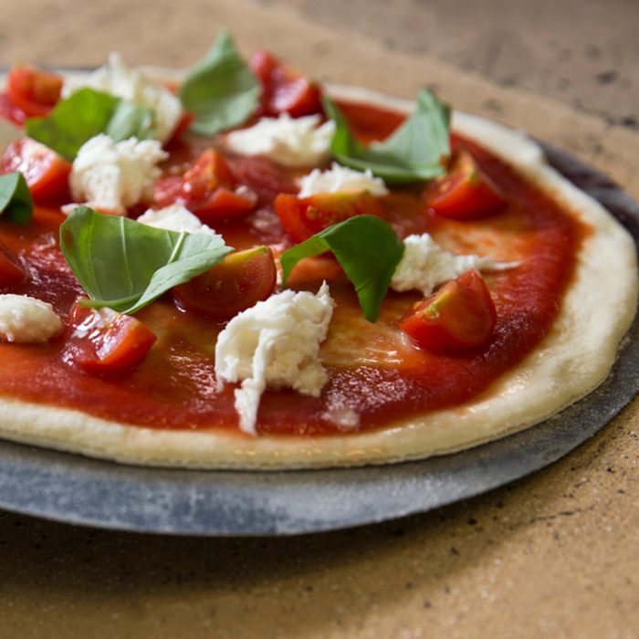 a raw pizza with tomato sauce, oil, buffalo mozzarella and fresh basilicum leafs ready to put in the oven on a refractory stone