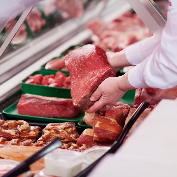 saleswoman offering fresh meat at display in supermarket