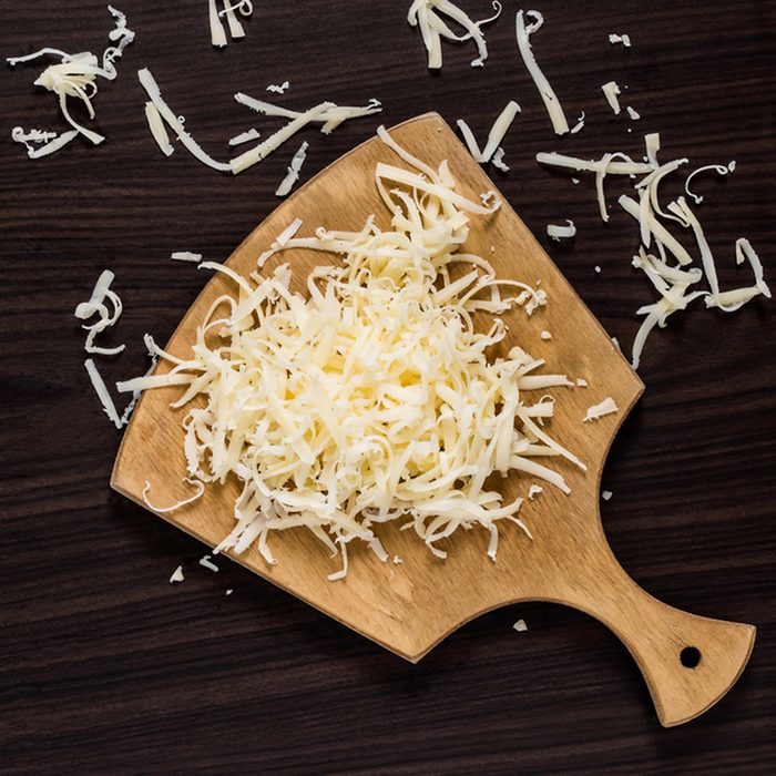 Grated cheese for cooking on a cutting board on a dark background.