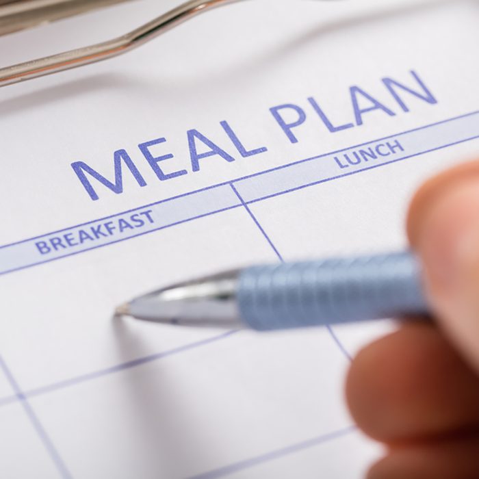 Close-up Of Person Hand Filling Meal Plan Form;