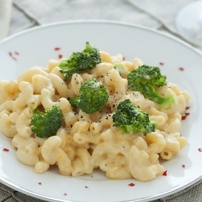 White plate of fresh homemade macaroni and cheese with broccoli and red pepper