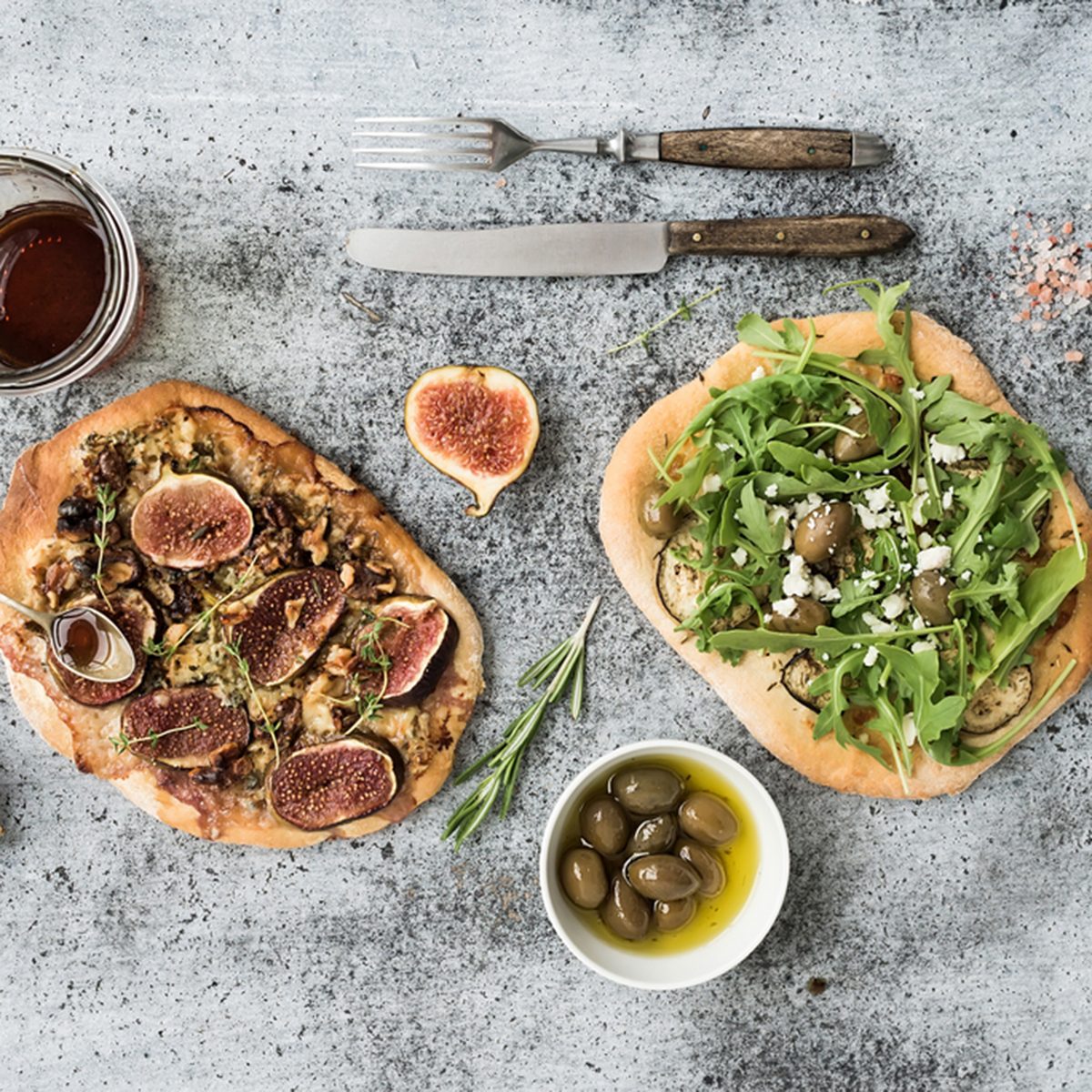 Rustic homemade pizzas with eggpant, cheese, olives, arugula, prosciutto and figs over grunge backdrop.
