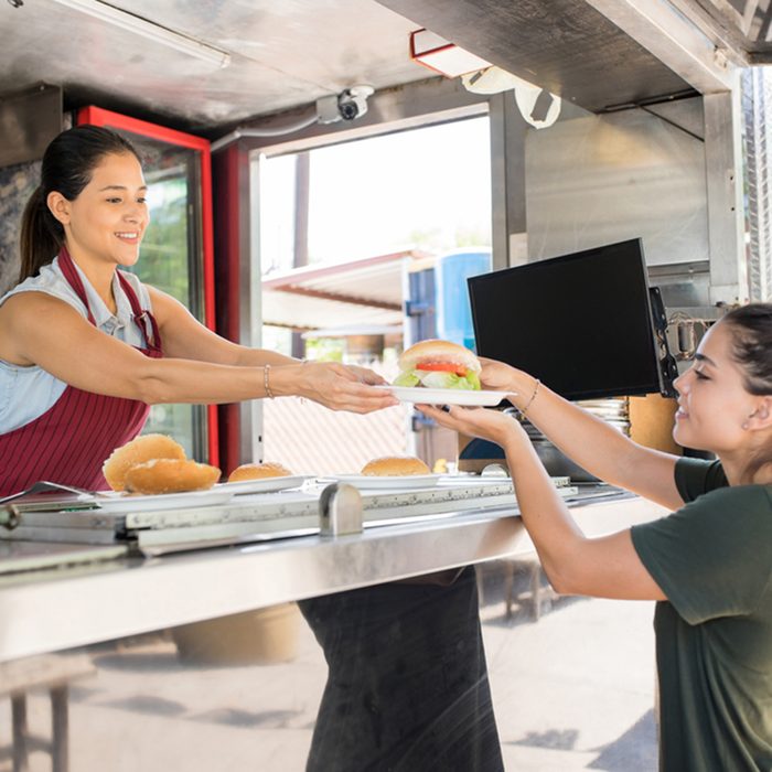 Profile view of a food truck worker handing over a hamburger to a customer and smiling