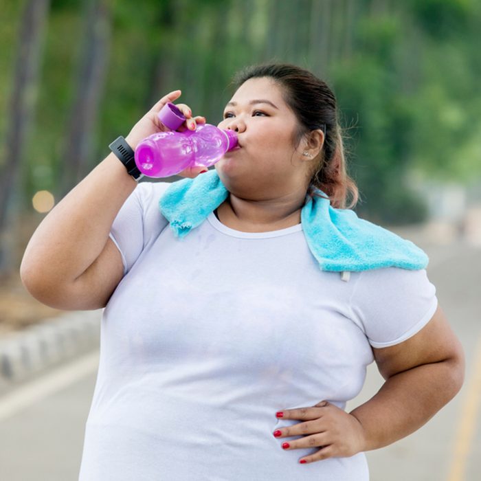 Picture of obese woman drinking water after jogging on the road