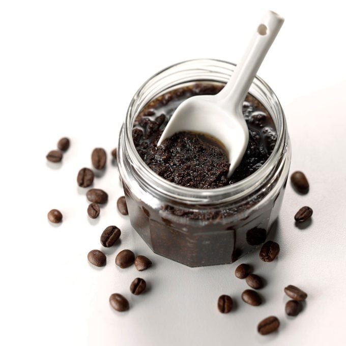 A jar of DIY coffee body scrub with scoop and coffee beans