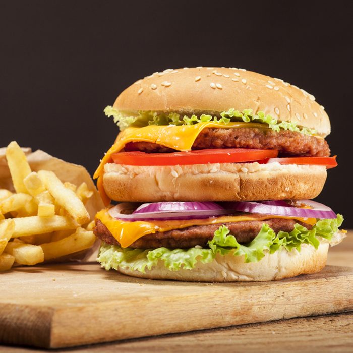 Fresh delicious double burger with cheese, tomato, onion, french fries and lettuce on wooden table and brown background