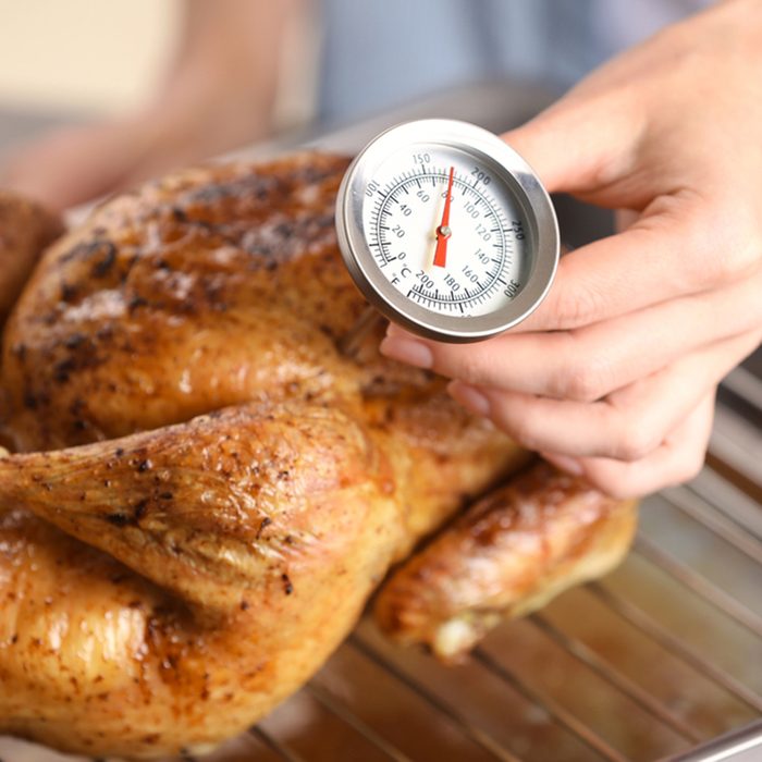 Young woman measuring temperature of whole roasted turkey with meat thermometer