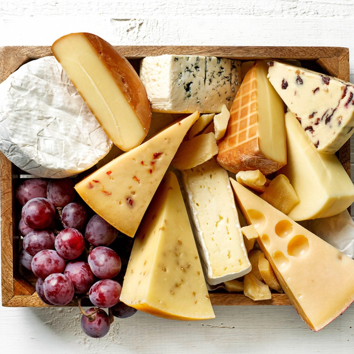 various types of cheese in wooden box on white wooden table