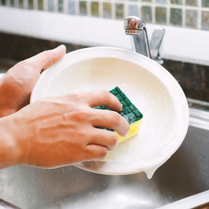 Close-up view of hands in rubber gloves washing dishes with sponge.