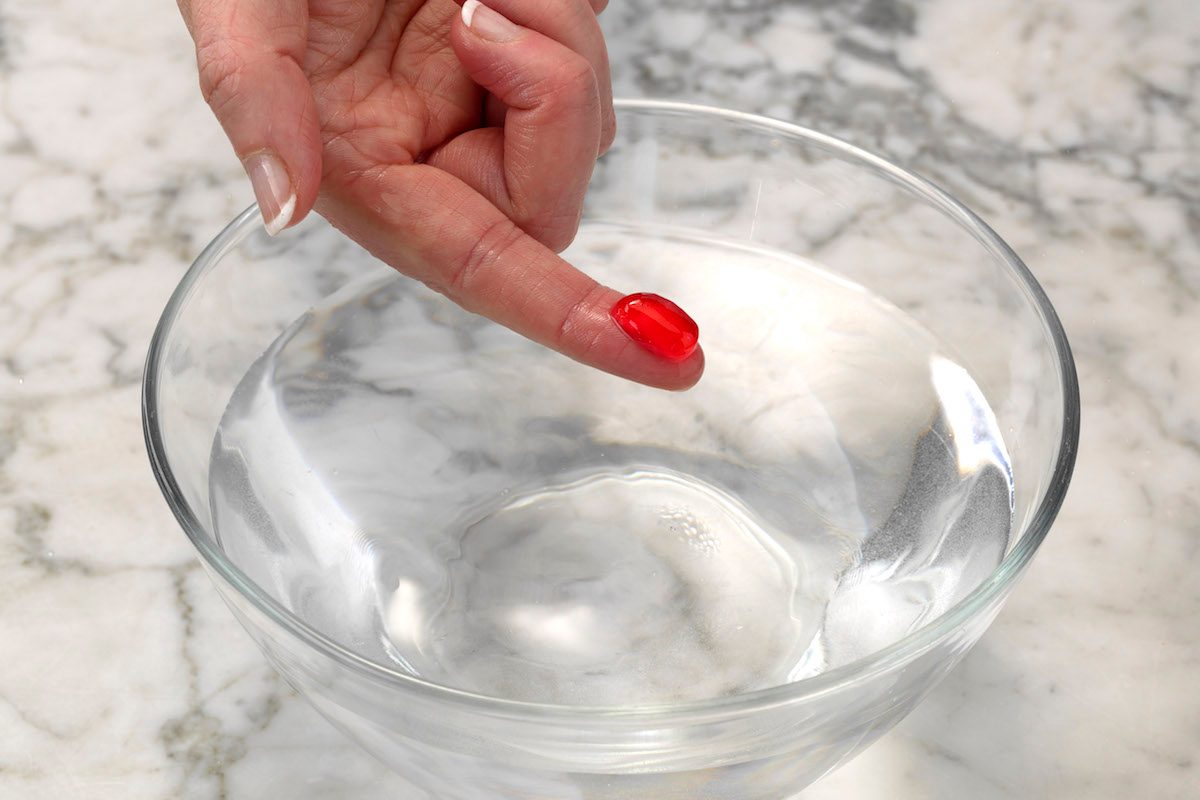 Testing red homemade candy using the cold water test. The mixture forms a ball when dipped in cold water and holds its shape after being removed, which means it's in firm-ball stage.