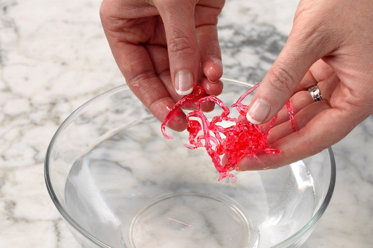 Testing red homemade candy using the cold water test. The candy formed threads when it touched cold water and became hard and brittle when it was removed from the water, meaning it's in hard-crack stage.