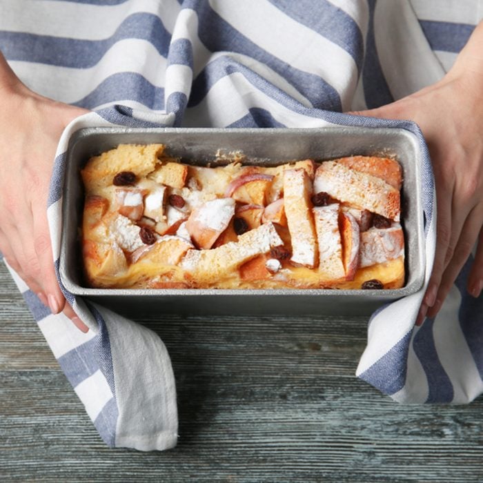 Female hands holding casserole dish with baked bread pudding on wooden table