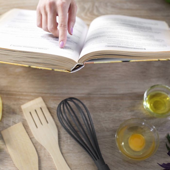 Lady reading pizza recipe in culinary book at home with kitchenware on table