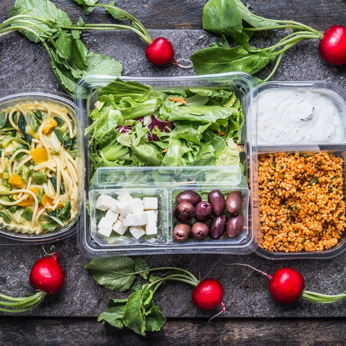 Variety of clean dieting salads in plastic package and green measuring tape on rustic background, top view.