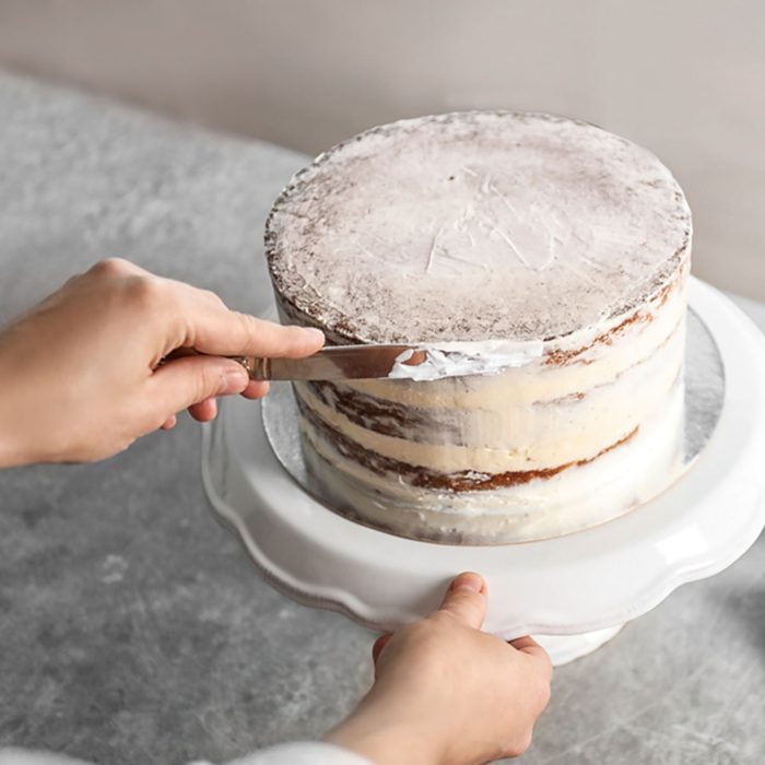 Woman decorating delicious cake with fresh cream on stand. Homemade pastry; Shutterstock ID 1174965469; Job (TFH, TOH, RD, BNB, CWM, CM): Taste of Home