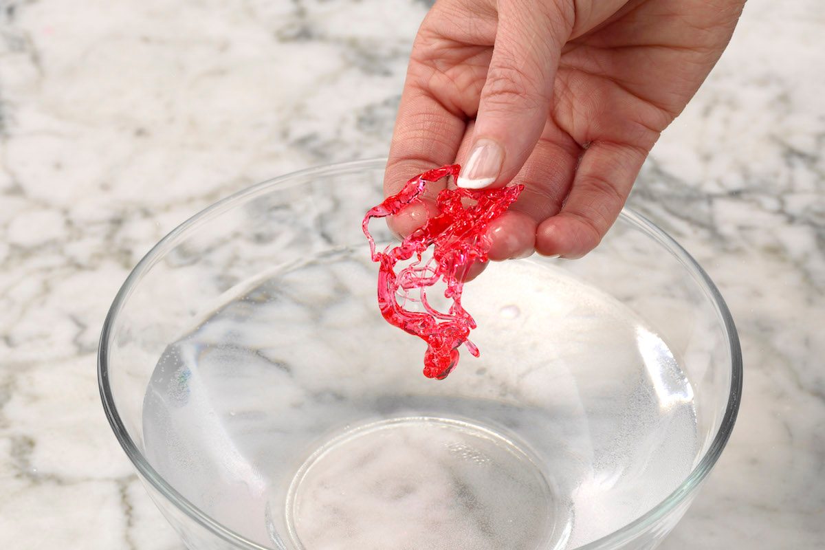 Testing red homemade candy using the cold water test. When cooled and removed from cold water, the candy will separate into threads that are hard but not brittle, meaning it’s in soft-crack stage.
