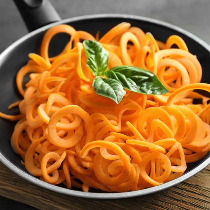Frying pan with raw carrot spaghetti on wooden board
