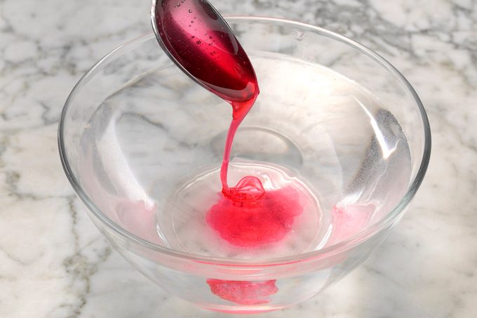 Testing red homemade candy using the cold-water test. The sugar is falling off a metal spoon in a fine thread, meaning it's in thread stage.