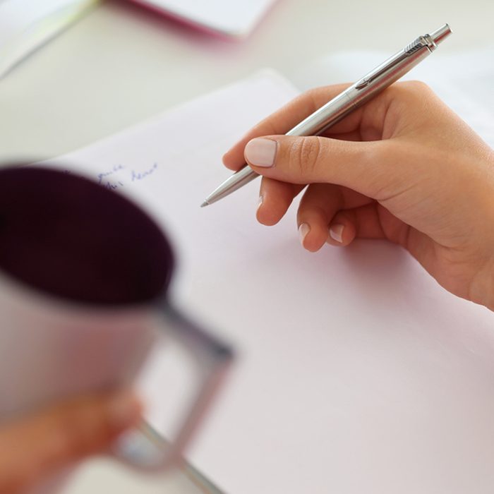 Female hands holding cup of coffee or tea and silver pen closeup.