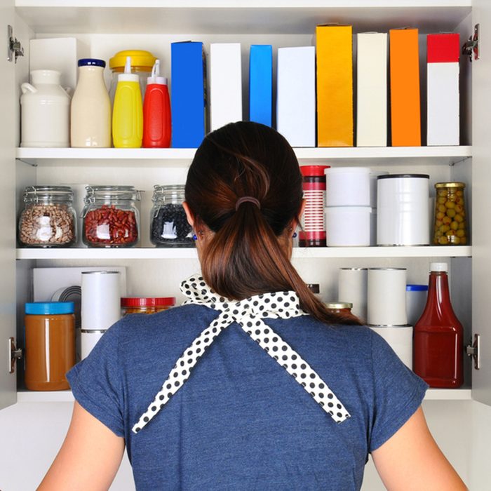 A woman seen from behind opening the doors to a fully stocked pantry.