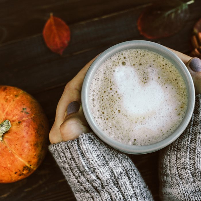 Cup of Spicy pumpkin latte in Woman's hands in gray sweater on the brown wooden table with red leaves. Cozy autumn mood; Shutterstock ID 472601899; Job (TFH, TOH, RD, BNB, CWM, CM): TOH
