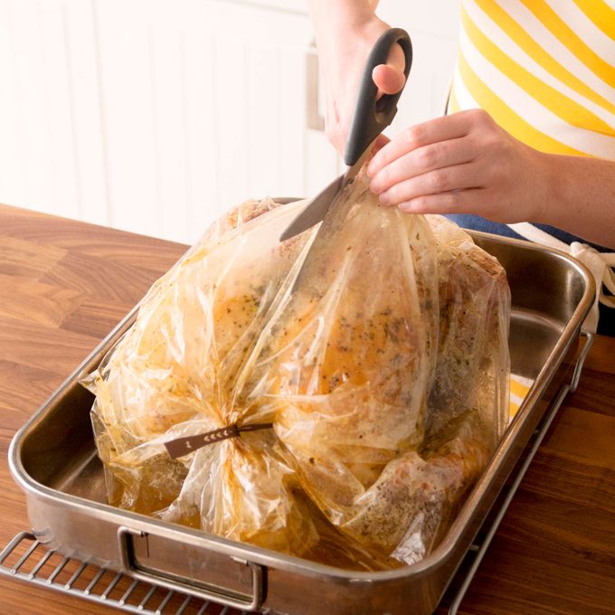 cutting open a turkey bag with a cooked turkey inside