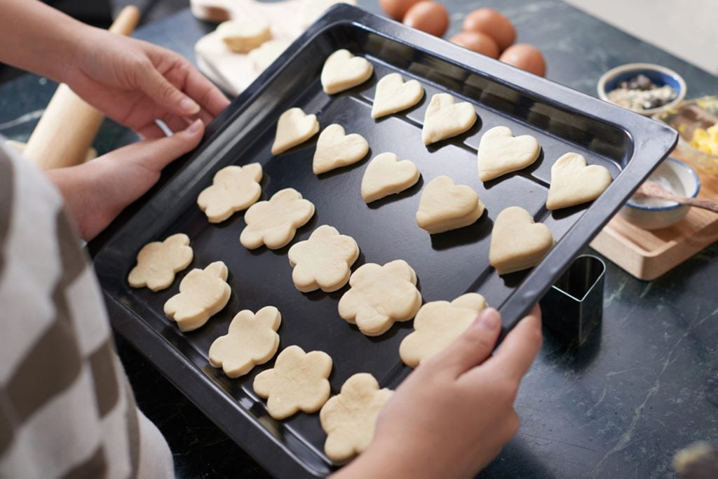 Close-up view of female hands holding baking sheet with cut out raw cookies of different shapes