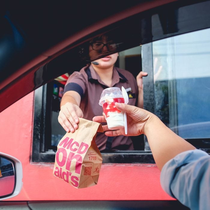 Unidentified customer receiving hamburger and ice cream after order and buy it from McDonald's drive thru service