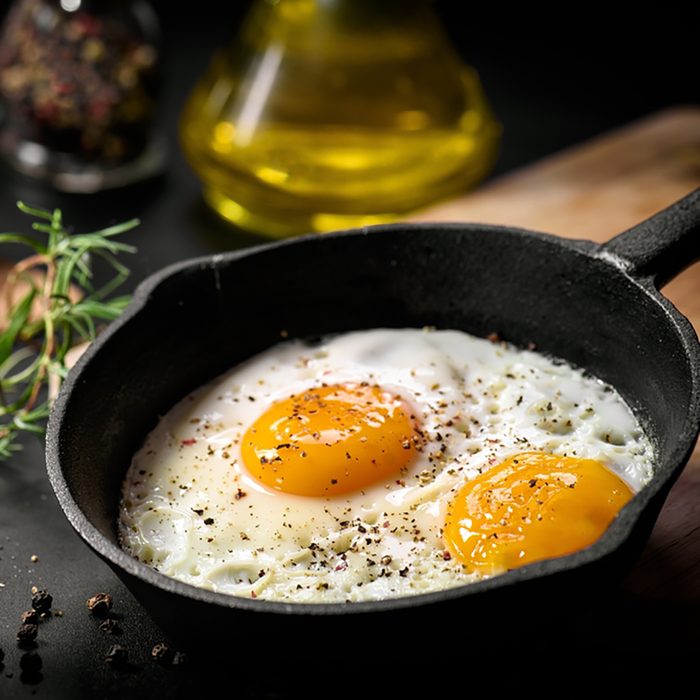 Fried eggs in a frying pan with cherry tomatoes and bread for breakfast on a black background