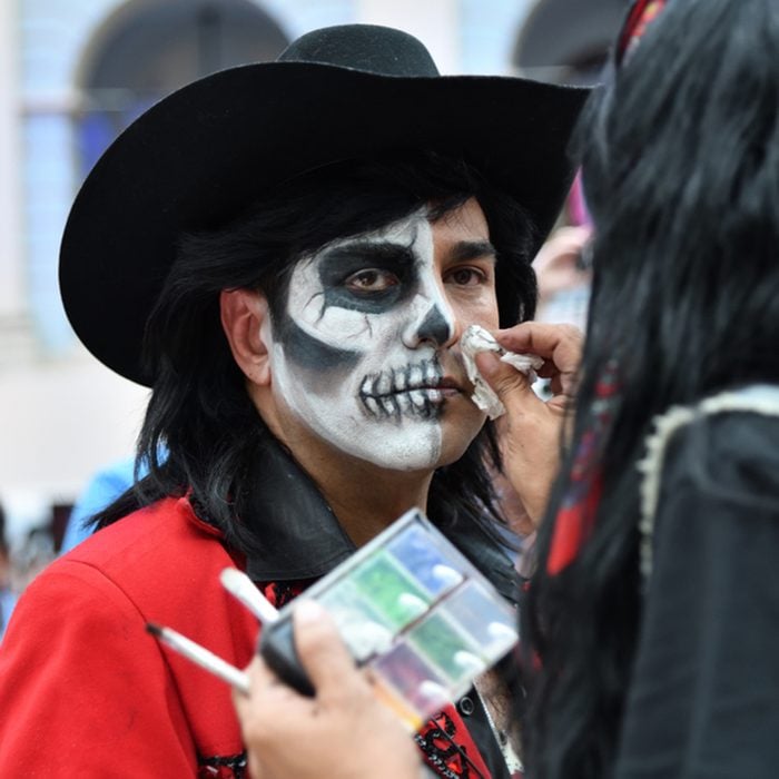 The girl makes the sugar skull makeup on face a man during Day of the dead
