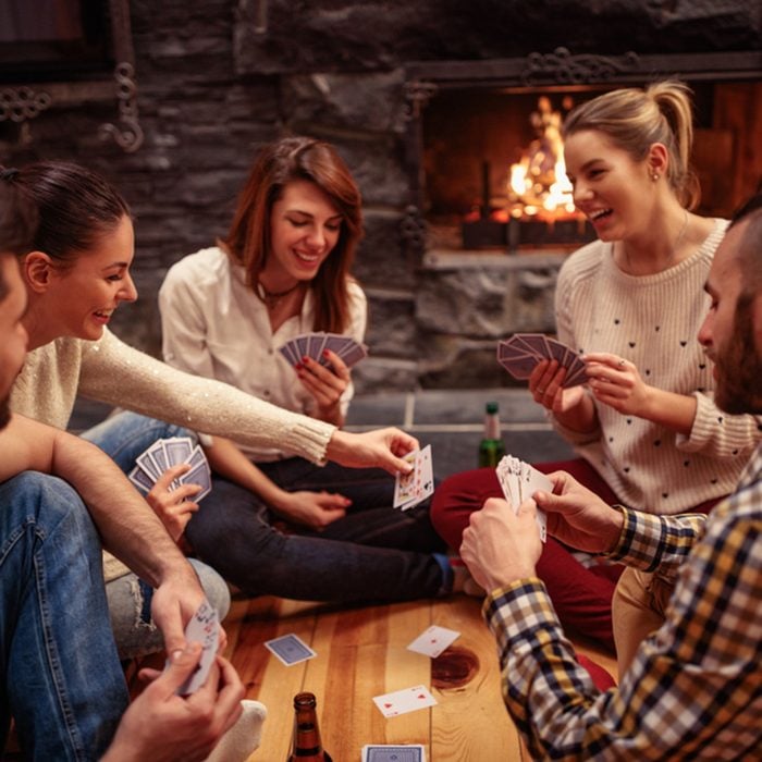 Young smiling friends partying together and playing cards