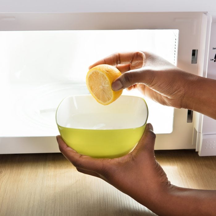 Human Hand Putting Sliced Lemon In Bowl Near Open Microwave