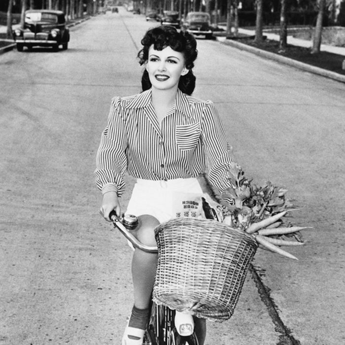 Young woman riding her bicycle with basket full of flowers and carrots; Shutterstock ID 100085855; Job (TFH, TOH, RD, BNB, CWM, CM): Taste of Home