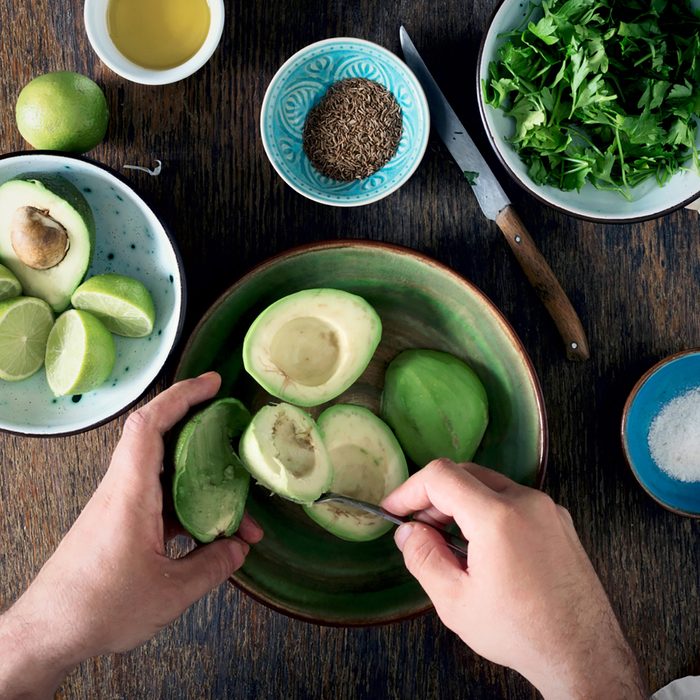 Cooking of Mexican guacamole sauce. Man preparing Mexican sauce guacamole on rustic wooden table