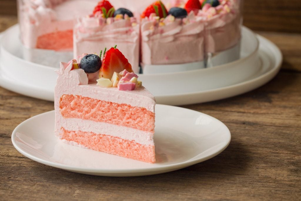 White chocolate strawberry yogurt cake decorated with fresh fruits and chocolate chunk on wood table.