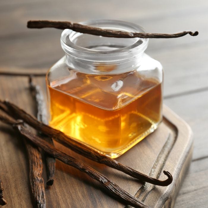 Jar with vanilla extract and sticks on wooden board