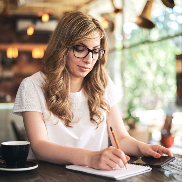 Woman writing on a notebook while holding her mobile phone