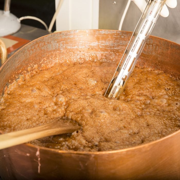Factory of the production of delicious caramel candies. First step. Boiling syrup of sugar in copper pot with thermometer and big spoon. Brown colour for the syrup.; Shutterstock ID 674437753; Job (TFH, TOH, RD, BNB, CWM, CM): TOH