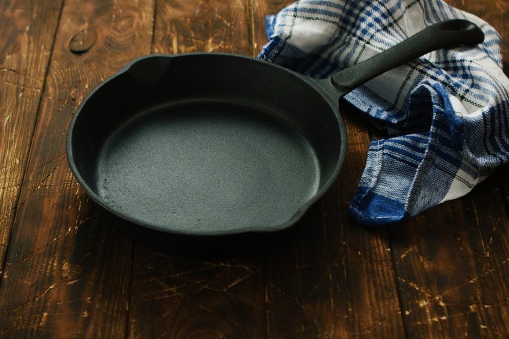 Simple black colored cast iron pan with checkered towel on wooden shabby table surface