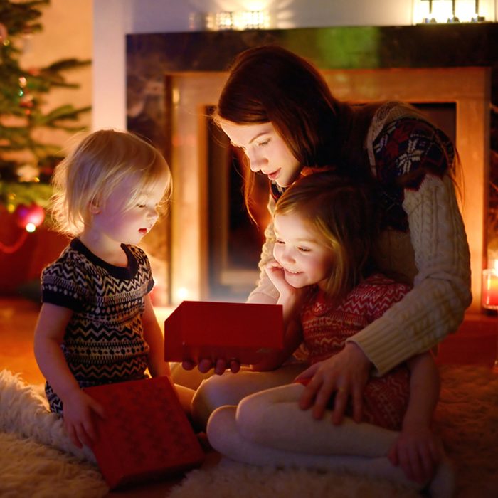 Young mother and her two little daughters opening a magical Christmas gift by a Christmas tree in cozy living room in winter; Shutterstock ID 212733760; Job (TFH, TOH, RD, BNB, CWM, CM): TOH