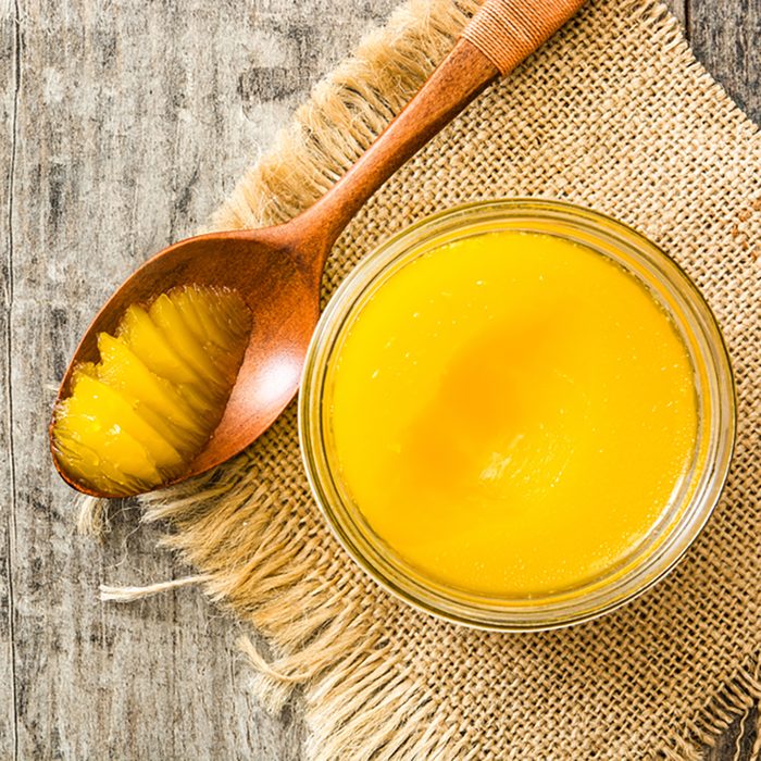 Ghee or clarified butter in jar and wooden spoon on wooden table.