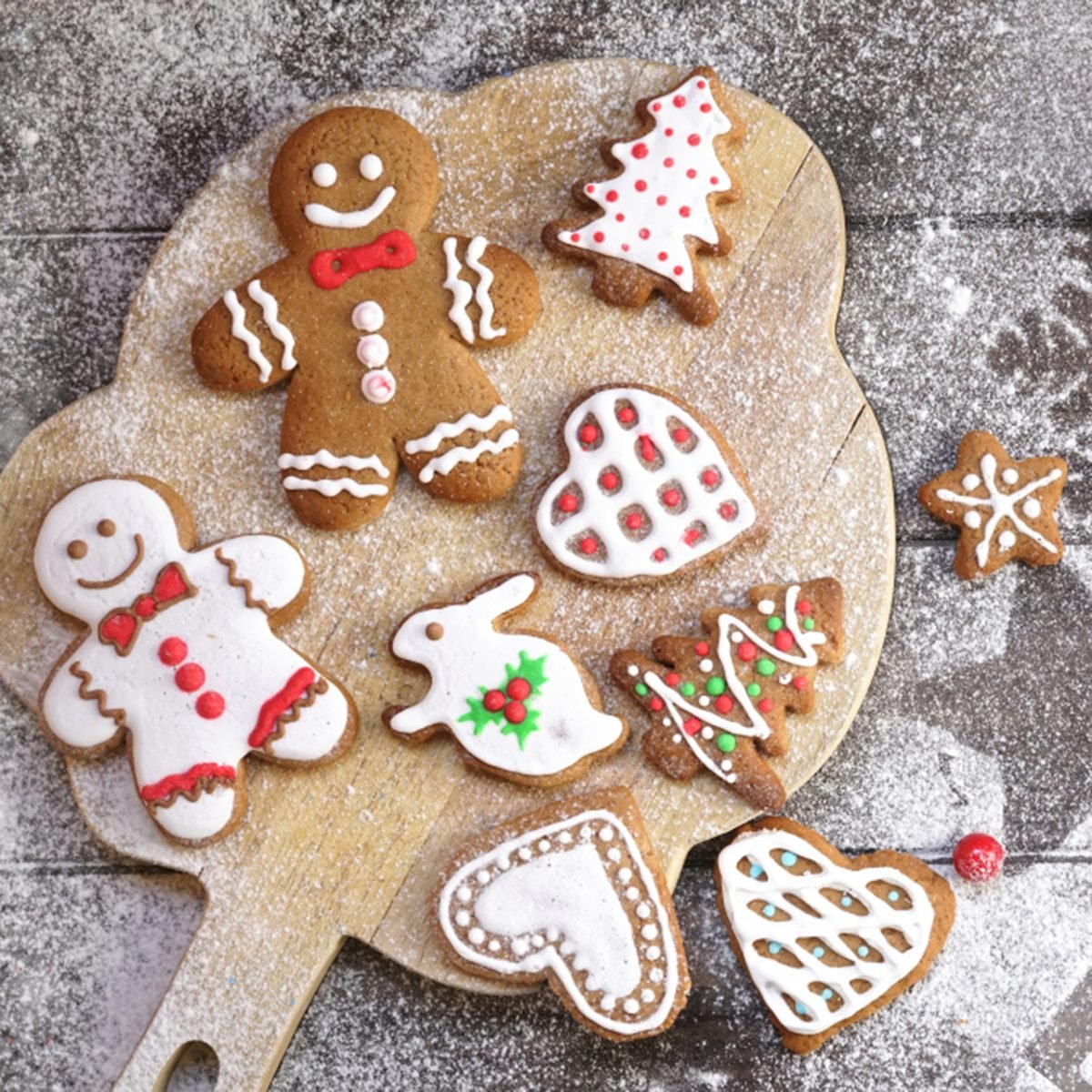Christmas cookies of various shapes in sugar glaze on a cutting board on a brown wooden table sprinkled with flour, flat lay.