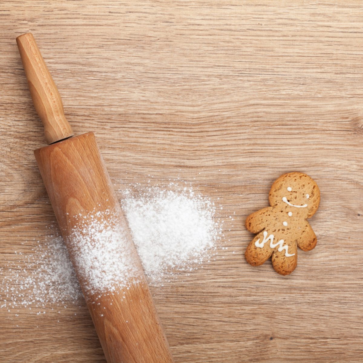 Rolling pin with flour and gingerbread cookie on wooden table.